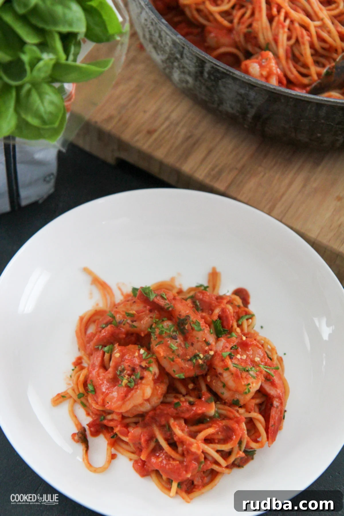 a white bowl with spaghetti and shrimp and basil on the side 