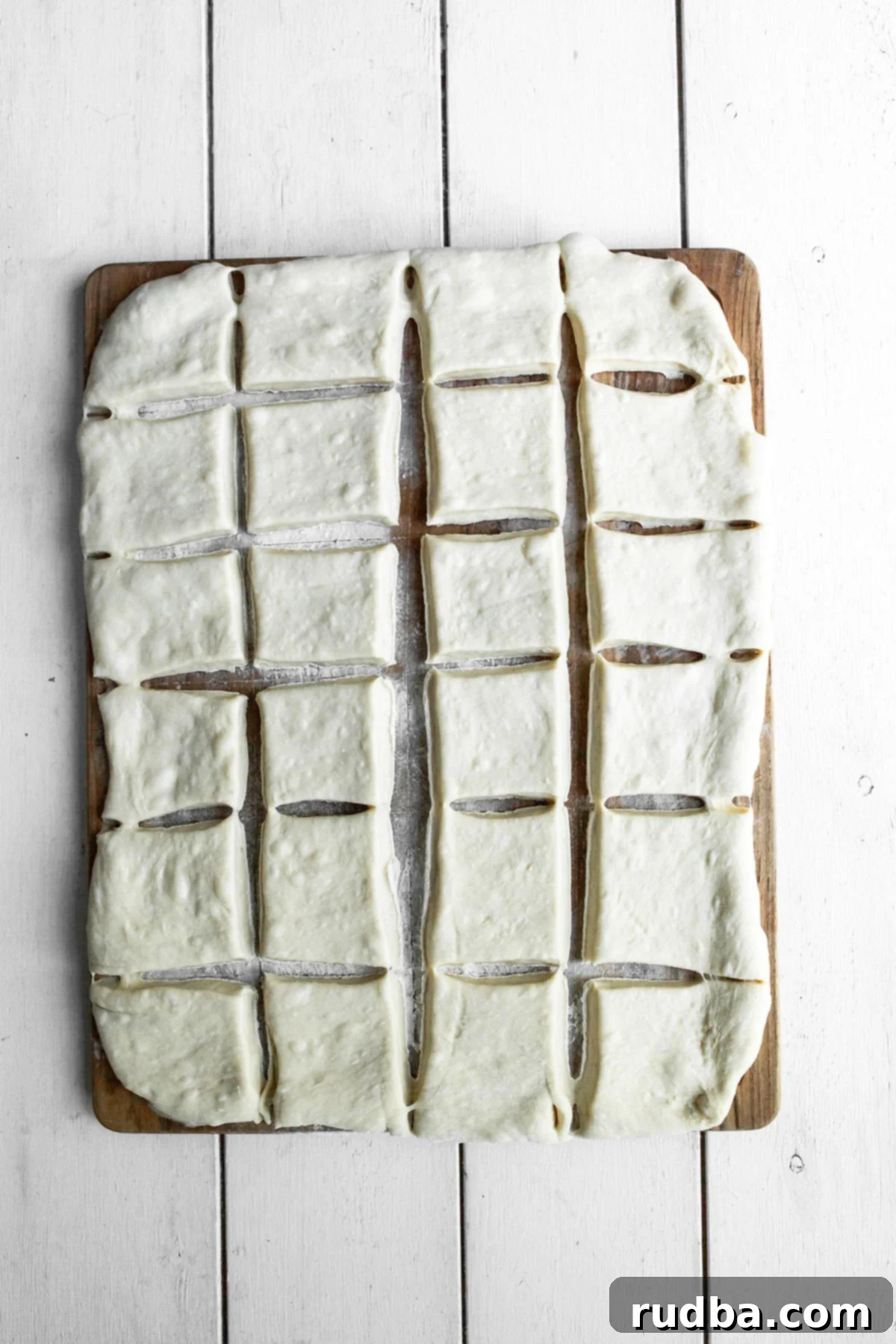 twenty four squares of raw dough on a wooden board.