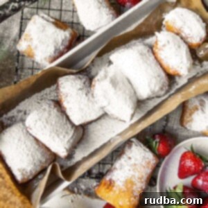 Pillowy Homemade Beignets 6 a long bog with brown paper and beignets inside. beignets on the side of the box along with strawberries and blueberries.