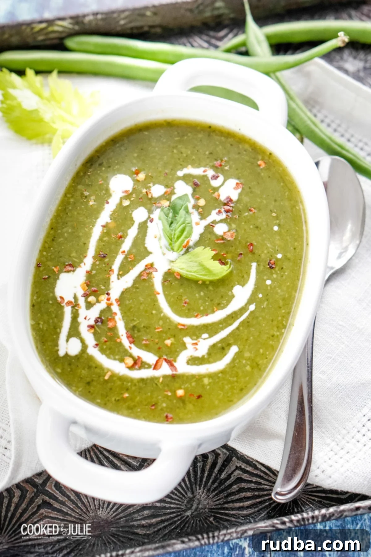 A creamy vegan green detox soup served in a white bowl, garnished with fresh herbs and a swirl of coconut milk.