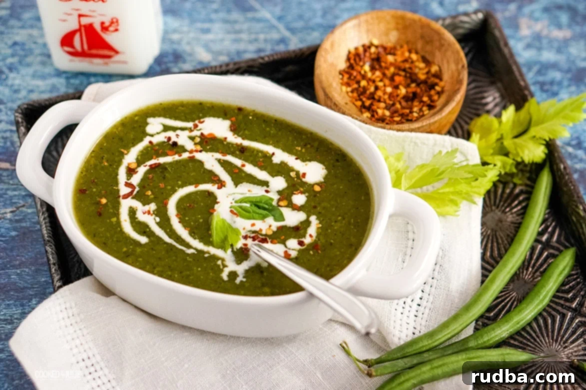 Close-up of a vegan green detox soup in a bowl, showing the vibrant green color, garnished with red crushed pepper and a few green beans on the side.