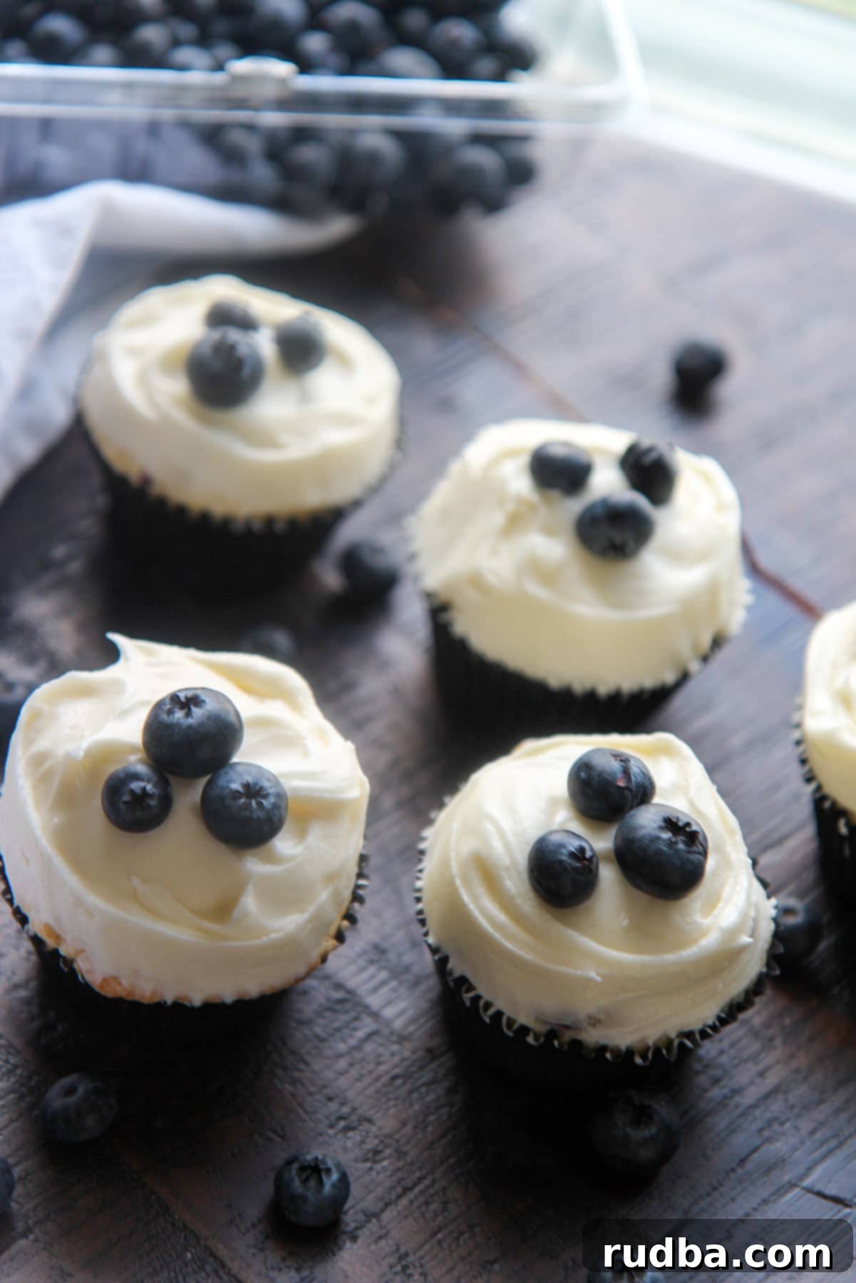 four cupcakes and fresh blueberries on the side 