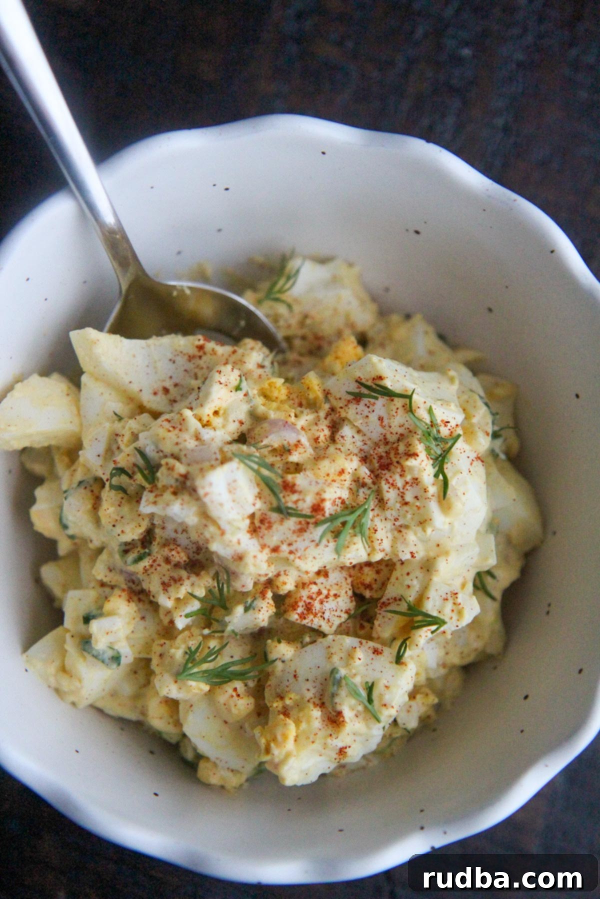 egg salad in a bowl with a spoon and paprika on top