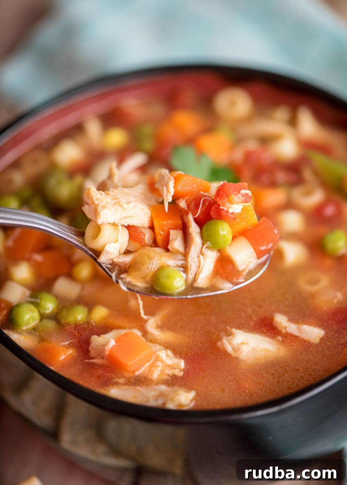 A close-up of a spoonful of chicken vegetable soup, with a blue kitchen towel in the background.