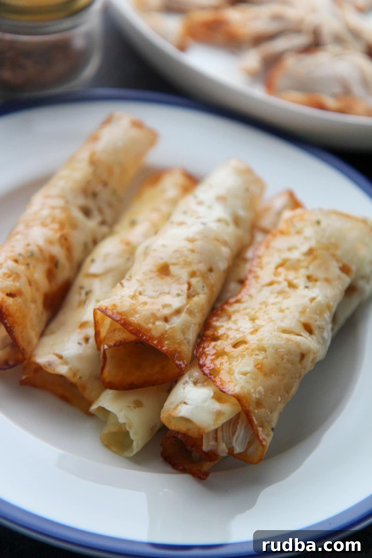 Six golden-brown keto cajun chicken taquitos arranged on a white and blue plate, ready to be enjoyed as a low-carb snack or meal.