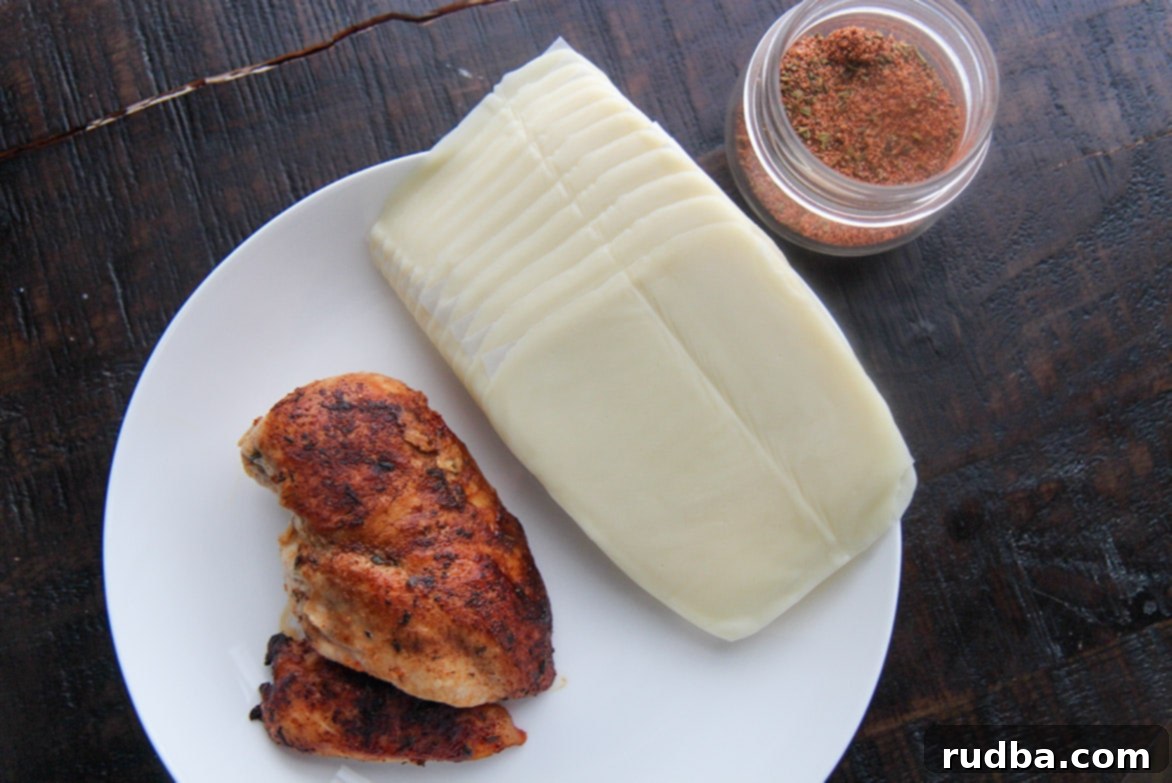 Cooked chicken breast, a jar of homemade Cajun seasoning, and a stack of mozzarella cheese slices, representing the three key ingredients for keto taquitos.
