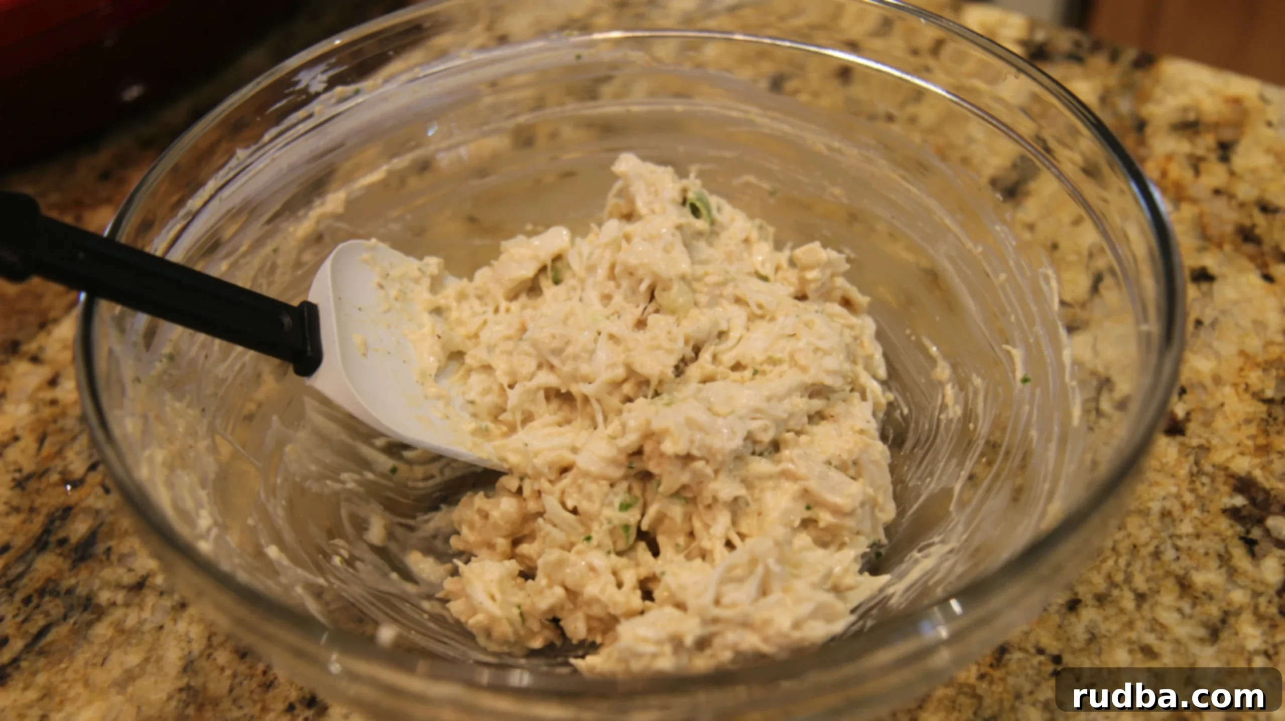 A bowl of creamy crab mixture, with visible chunks of crab meat, being gently folded to preserve its delicate texture.