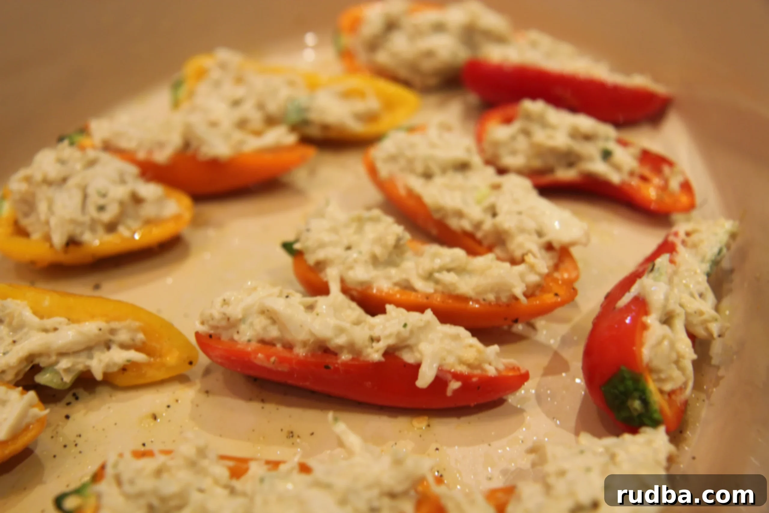 Mini peppers, halved and deseeded, ready to be filled, with a light drizzle of olive oil, salt, and pepper on a baking sheet.