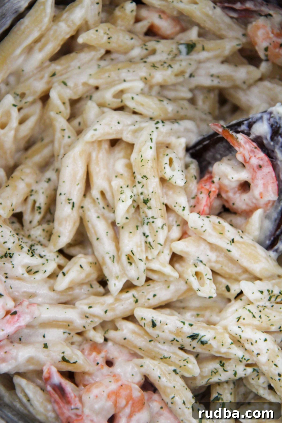 Shrimp and pasta covered in sauce with parsley and a wooden spoon up close.
