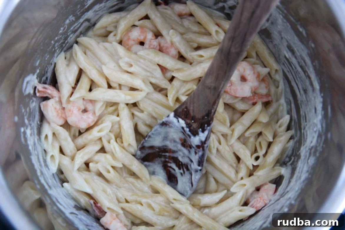 shrimp alfredo penne pasta with a wooden spoon in the instant pot. 