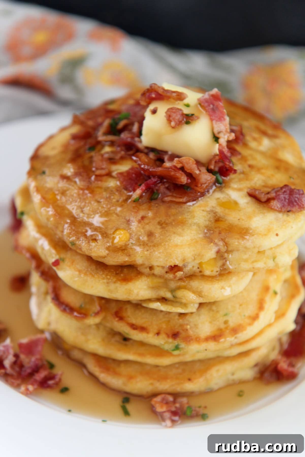 a short stack of bacon and corn pancakes on a white plate with syrup on top.