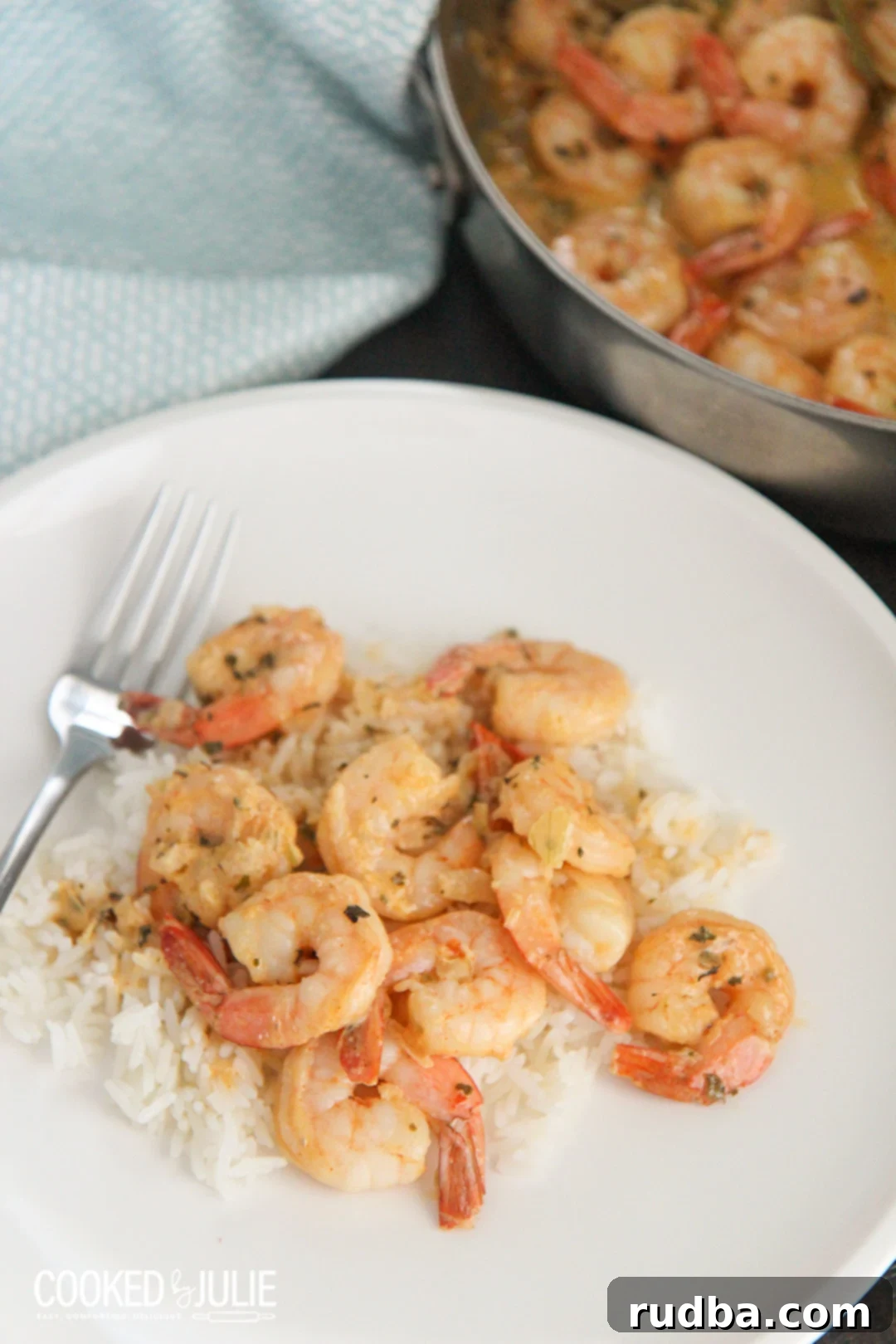Plump New Orleans style shrimp served over a bed of white rice on a clean white plate with a fork, garnished with fresh parsley.