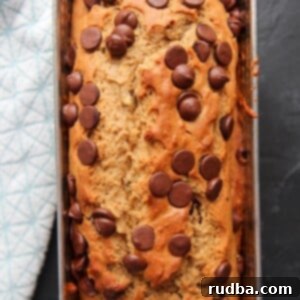 Moist Chocolate Chip Banana Bread 7 chocolate chip banana bread in a load pan on a black surface with a blue towel on the side.