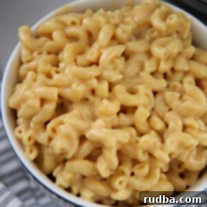 The Ultimate Instant Pot Mac and Cheese 5 mac and cheese in a white bowl with a gray and white towel on the side.