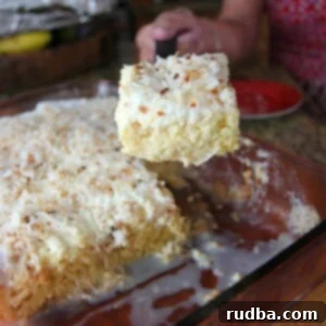 a hand lifting a slice of coconut tres leches and a full cake in the background.
