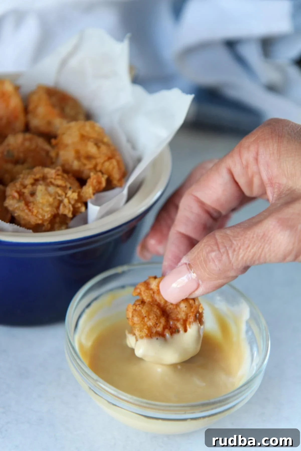 a hand dipping a fried shrimp in a honey mustard sauce. 
