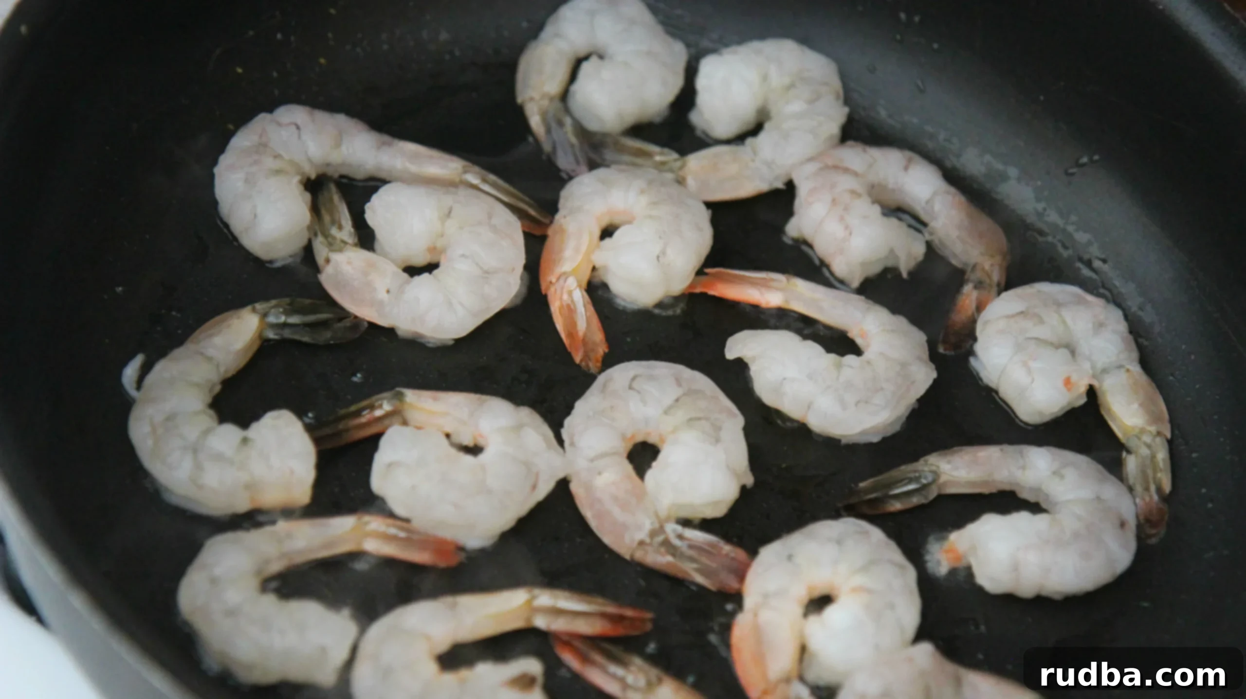 Raw shrimp in a black skillet cooking. 