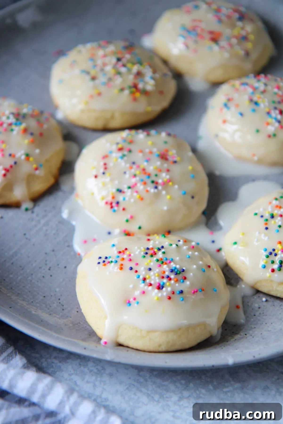 Seven glazed Italian lemon ricotta cookies with colorful sprinkles on a gray plate, showcasing their soft texture.