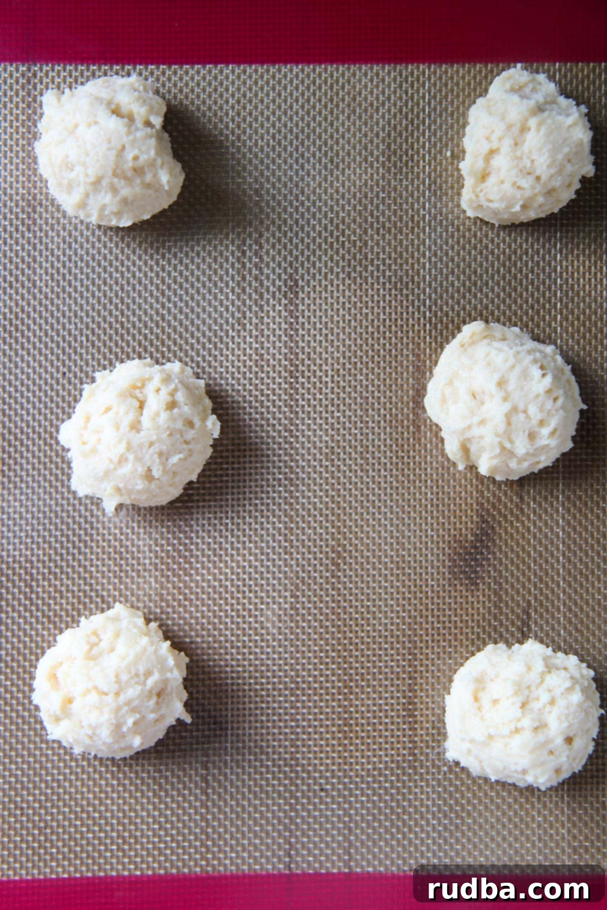 Six balls of sticky Italian lemon ricotta cookie dough carefully scooped onto a parchment-lined baking sheet, ready for baking.