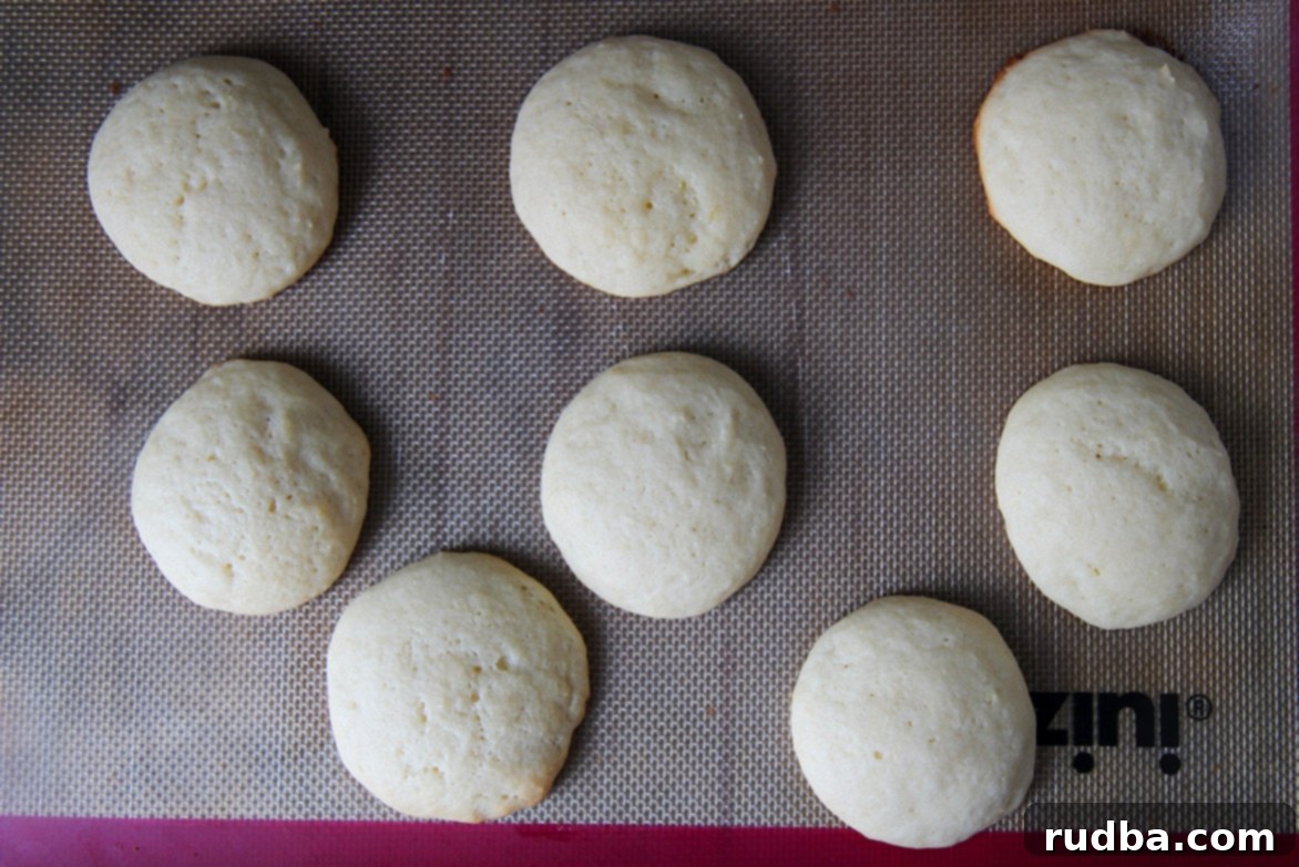 Eight soft-baked Italian lemon ricotta cookies cooling on a baking sheet, golden and ready for glazing.