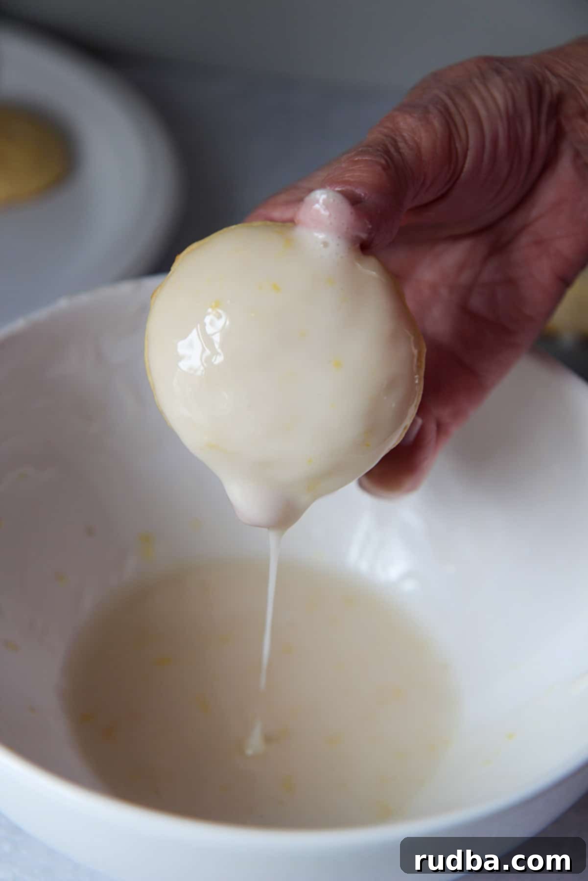 A hand dipping a soft-baked Italian lemon ricotta cookie into a white bowl filled with creamy lemon glaze.