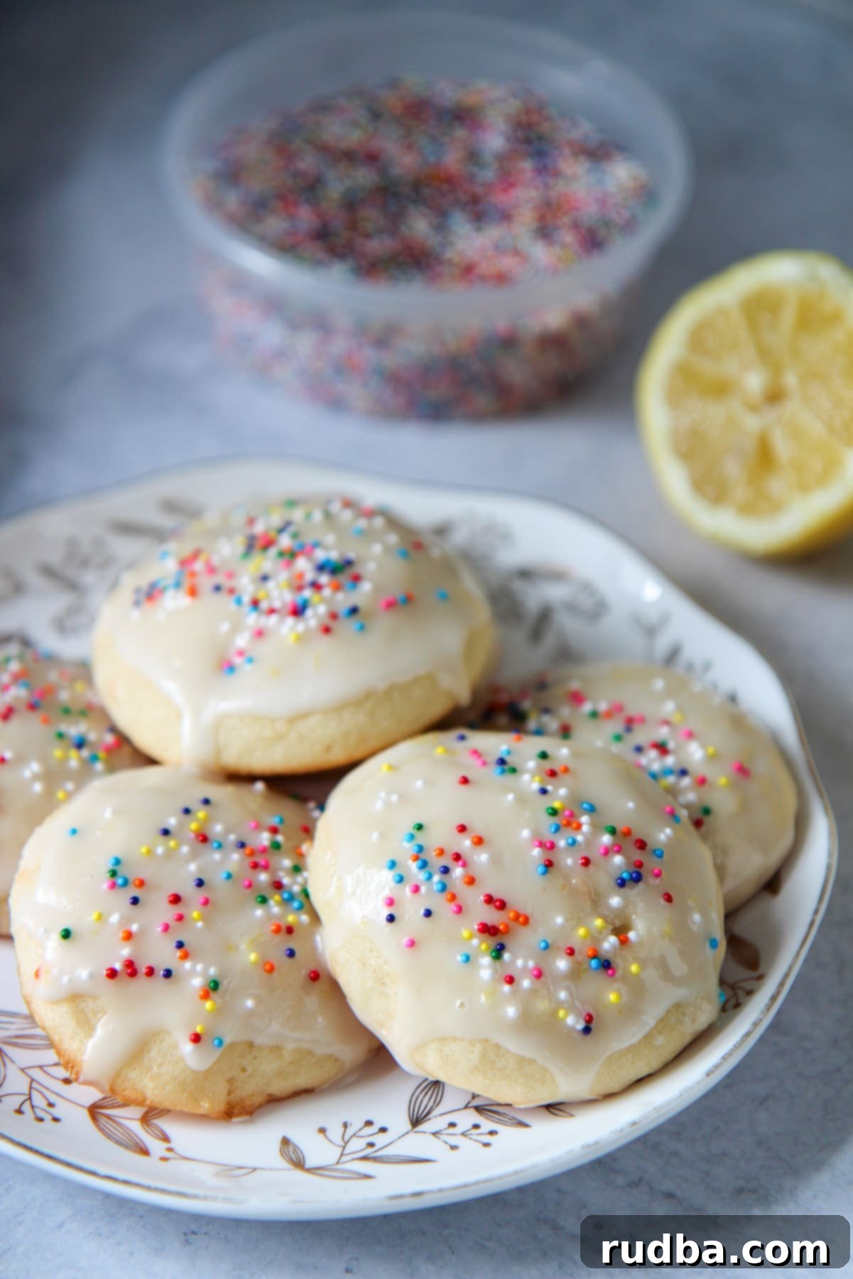A small plate showcasing several soft-baked Italian lemon ricotta cookies, adorned with sprinkles, with a fresh lemon in the background.