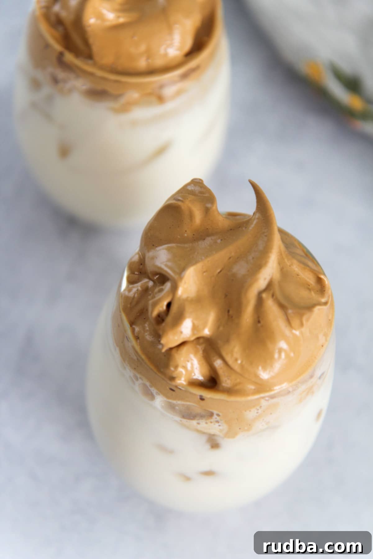 Two glasses filled with ice, milk, and light brown coffee foam on a gray surface, ready to be enjoyed.