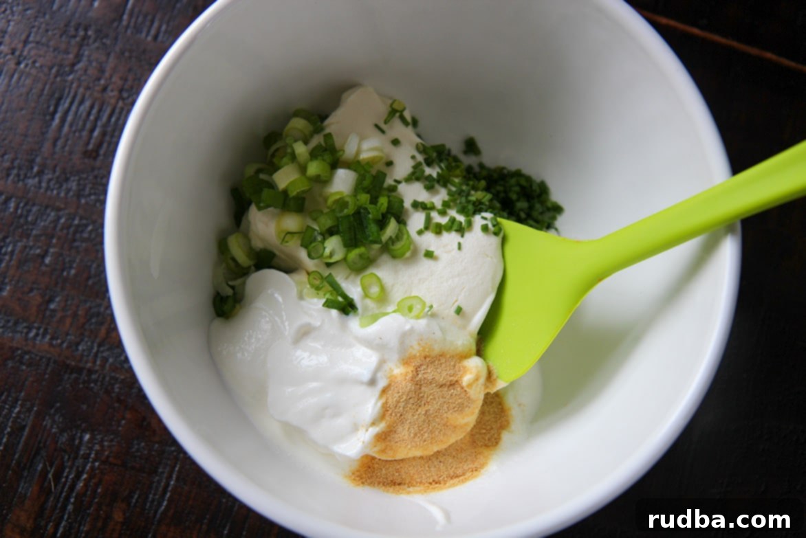 cream cheese, sour cream, granulated garlic, chives, scallions, and a green spatula in a white bowl. 