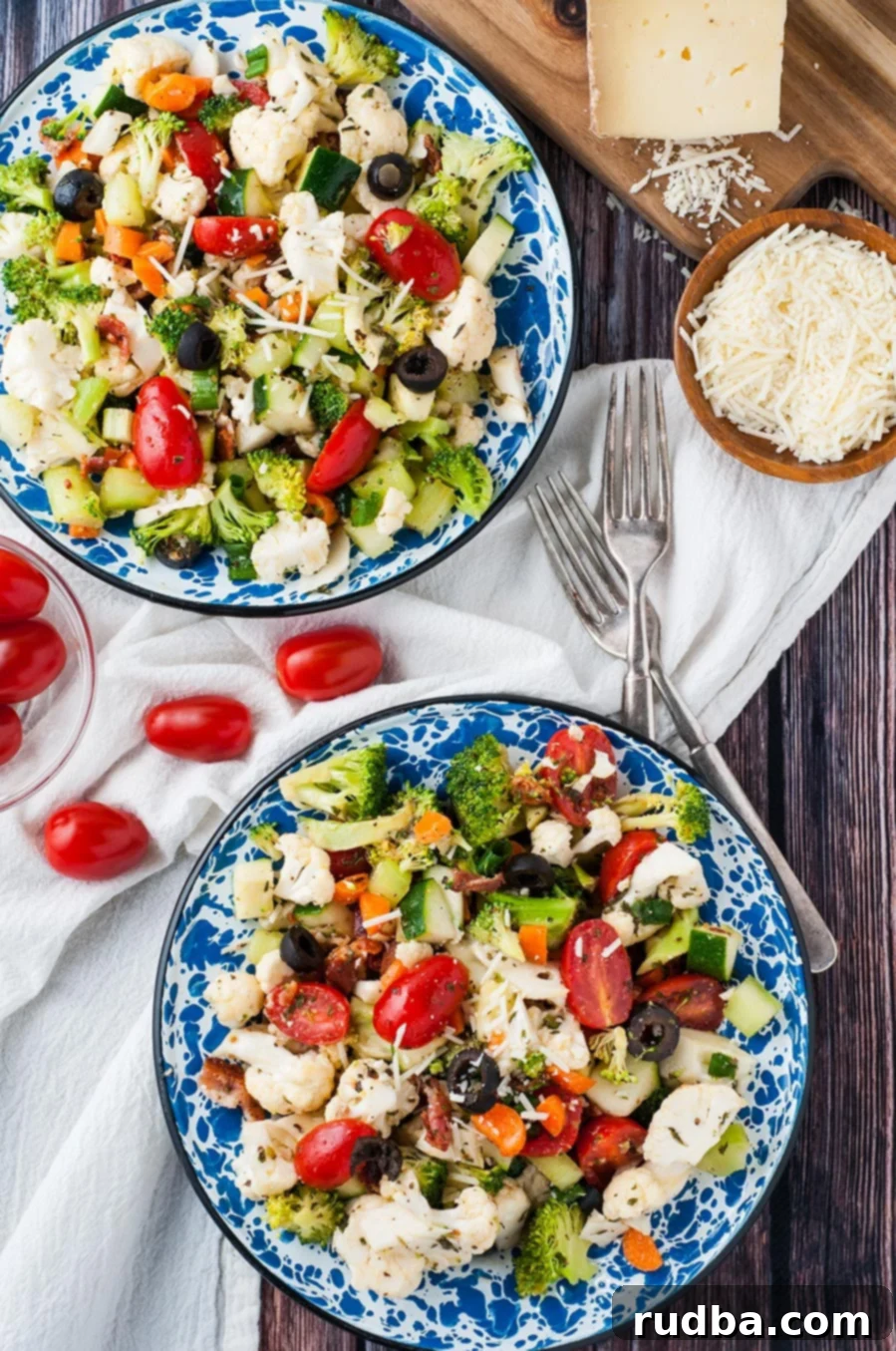 two bowls filled with vegetable salad with homemade Italian dressing. Two forks on the side and parmesan cheese.