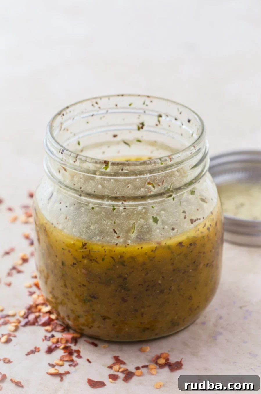 a small mason jar with dressing in it. Red crushed pepper and a lid on the side.