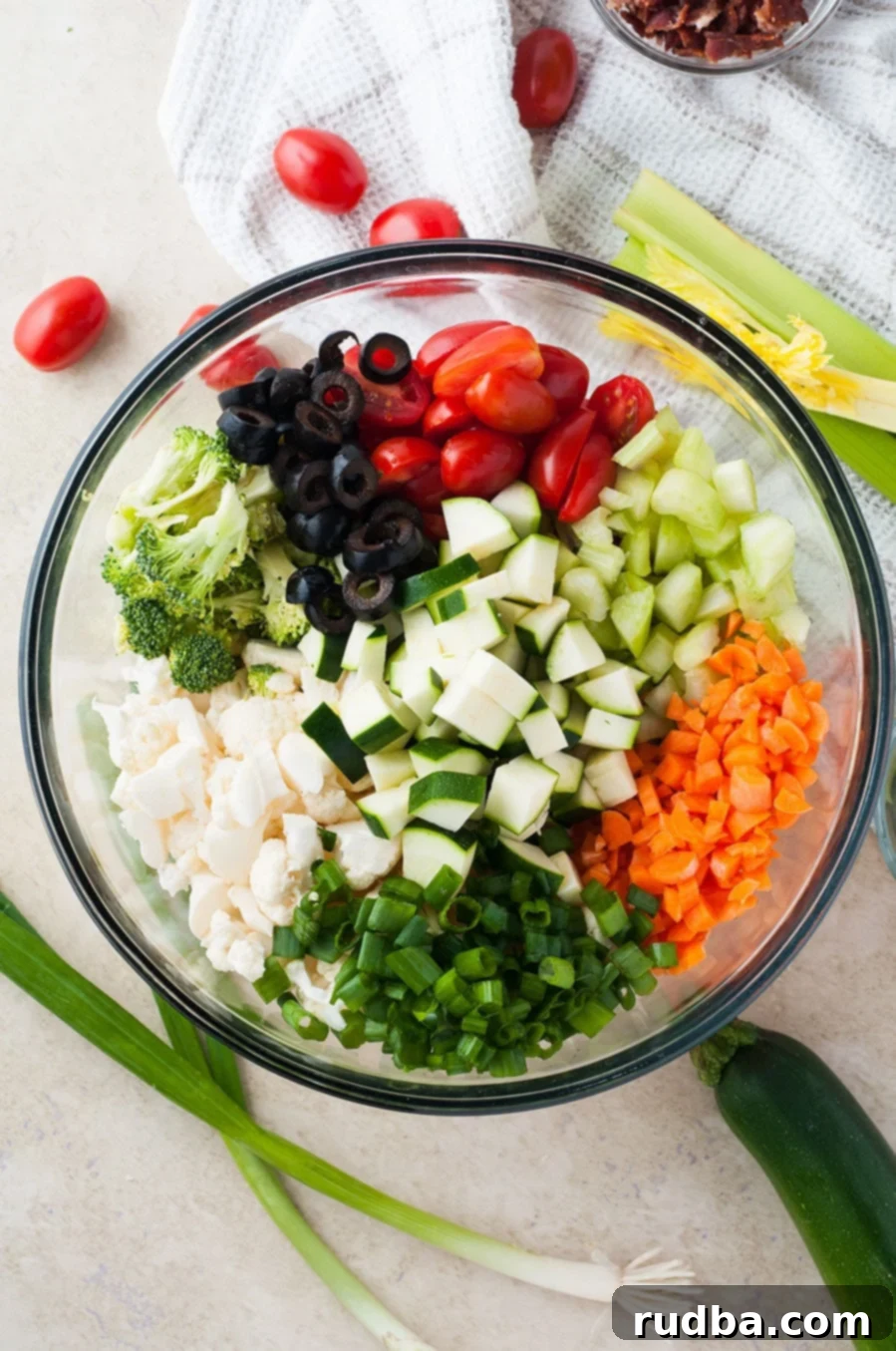 a large bowl filled with carrots, zucchini, broccoli, black olives, tomatoes, and cauliflower.