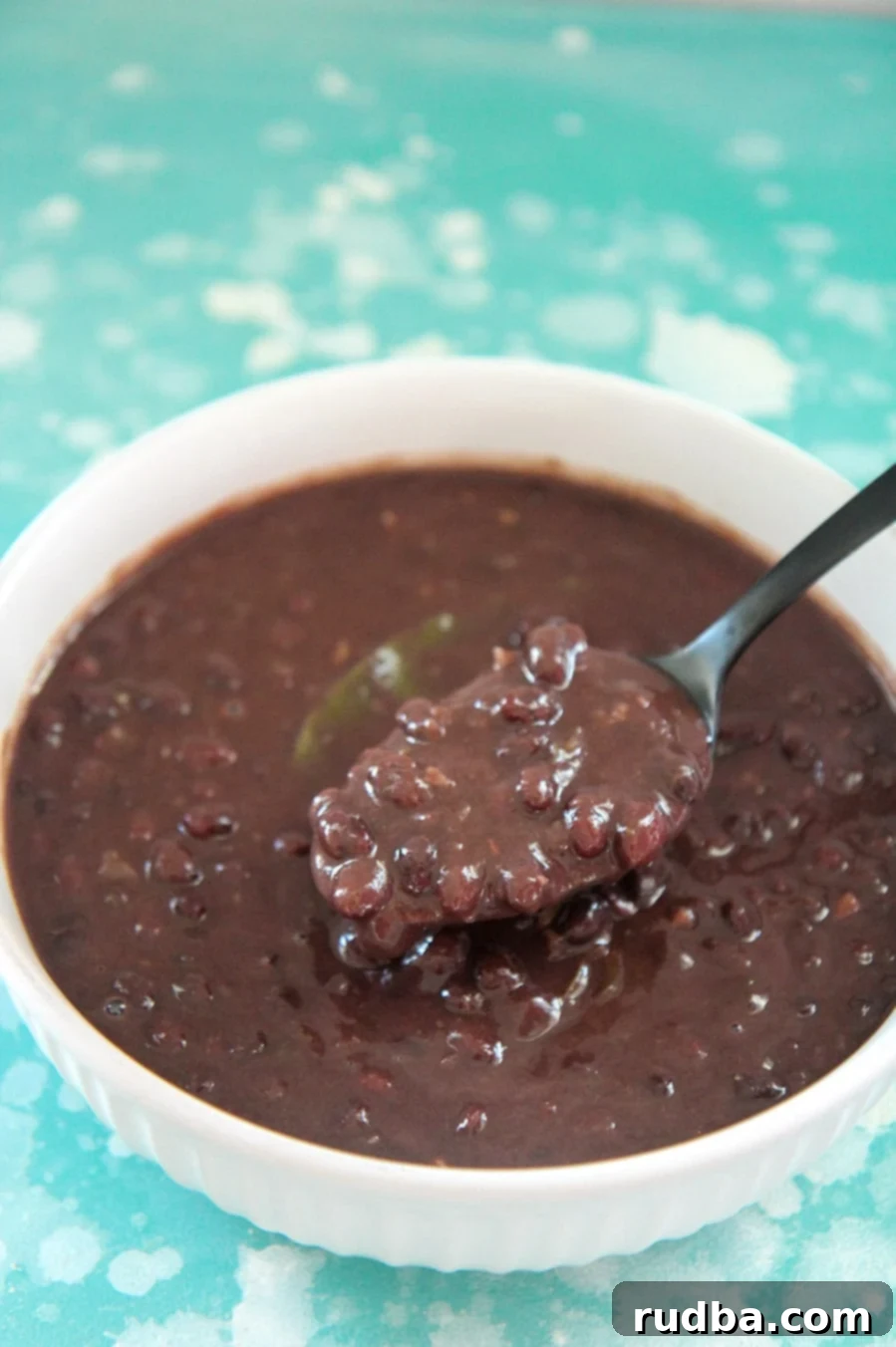 Cuban black beans in a white bowl with a black spoon. On top of a blue and white surface.