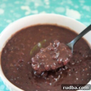 Easy Instant Pot Cuban Black Beans 5 Cuban black beans in a white bowl with a black spoon. On top of a blue and white surface.