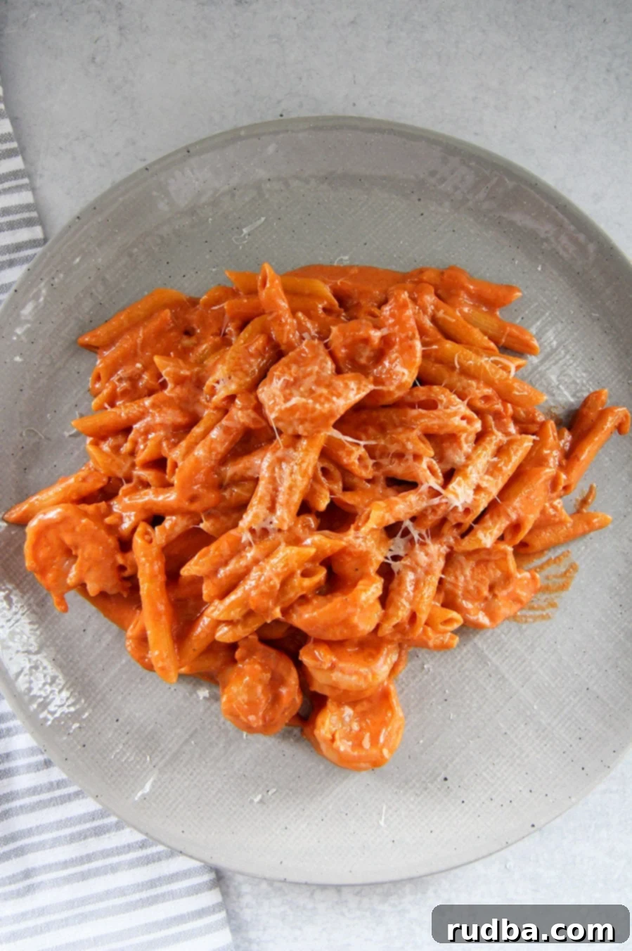 penne alla vodka with shrimp on a gray plate with a gray and white towel on the side. 