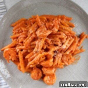 Creamy Vodka Penne with Shrimp 4 penne alla vodka with shrimp on a gray plate with a gray and white towel on the side.