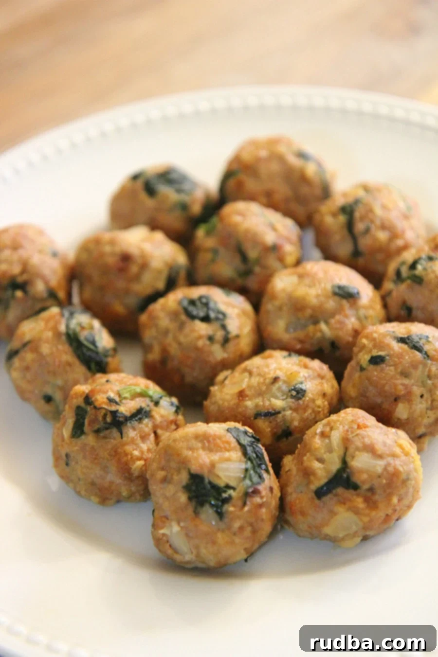 Fifteen perfectly baked spinach and turkey meatballs arranged on a pristine white plate, garnished with fresh parsley.