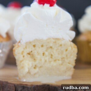 The inside of a tres leches cupcake with whipped cream and a cherry on top. Placed on a wooden surface.