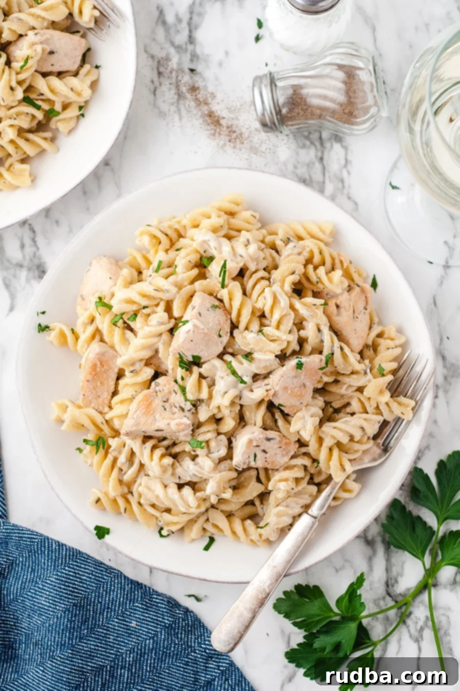 chicken and pasta in a white bowl with a fork and a blue towel on the side. 