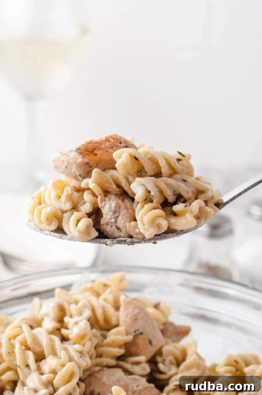 a spoon lifting pasta and chicken out of a bowl. 