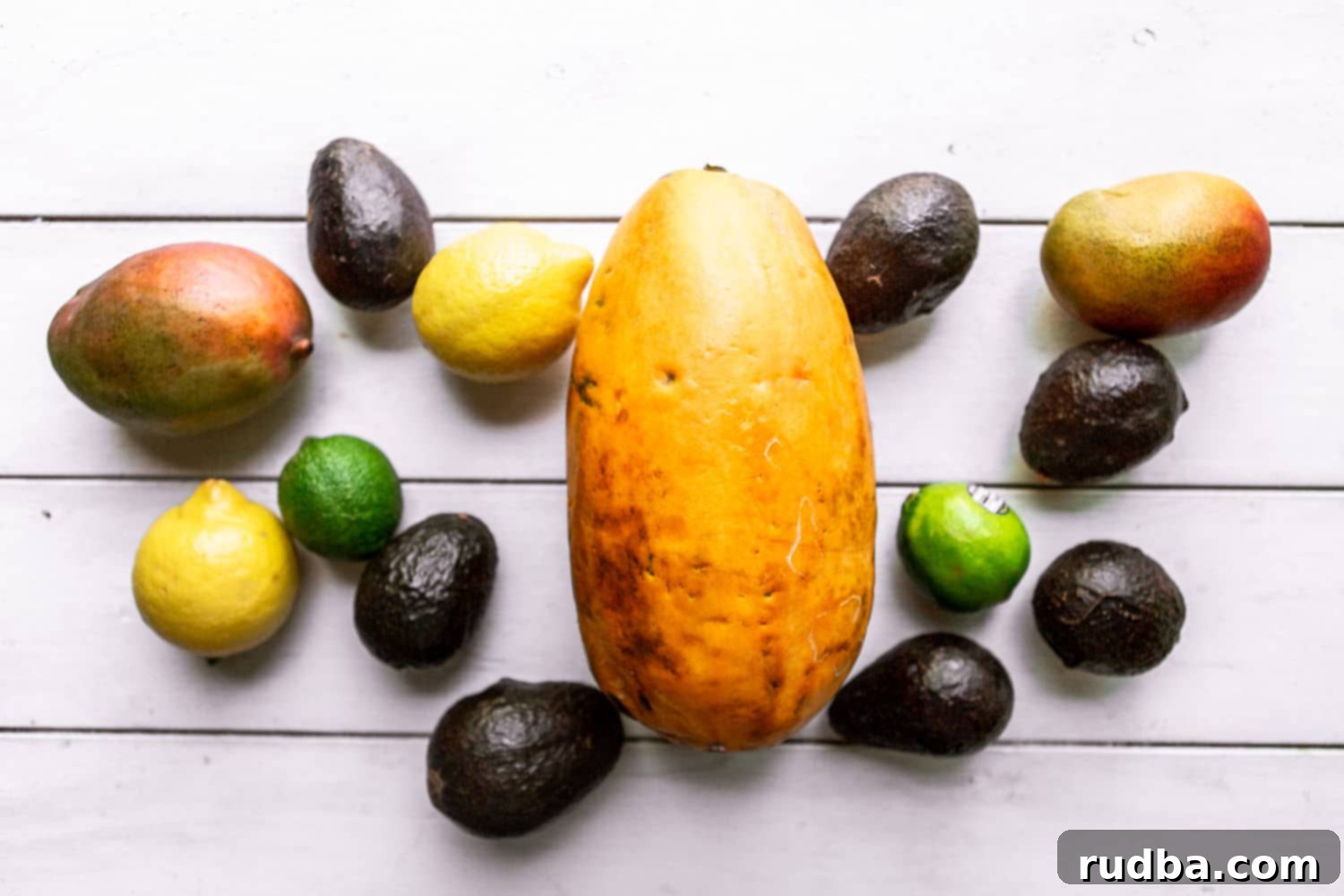 papaya, mangoes, avocados, lemons, and limes on a white surface.