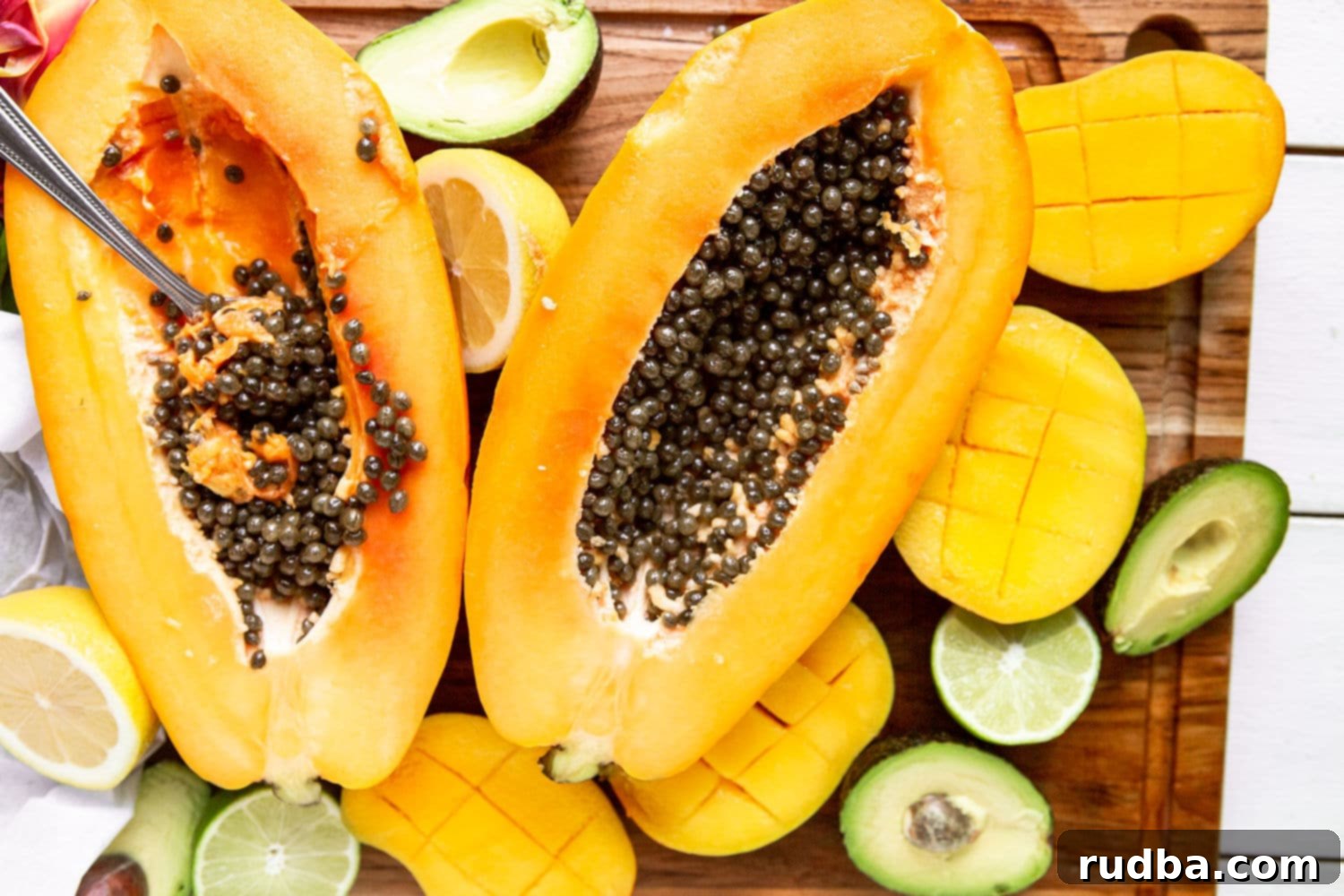 a papaya cut in half with avocados and mangoes on the side. 