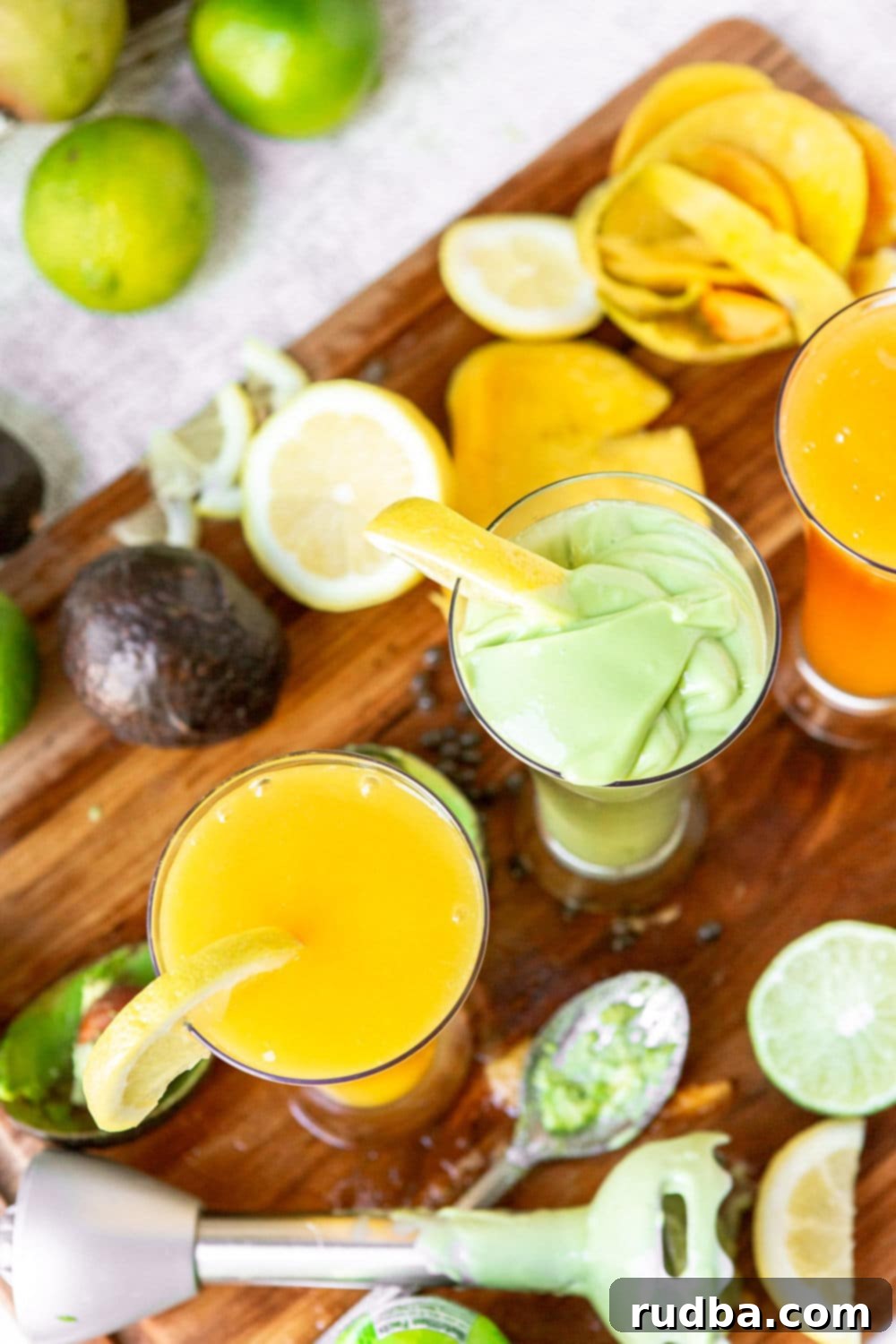 two glasses filled with a green and yellow juice with an immersion blender on the side. 