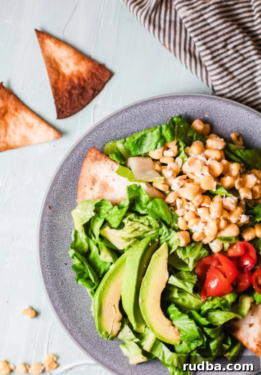 A beautifully presented blue bowl featuring a base of crisp lettuce, vibrant Mexican corn salad, juicy tomatoes, and creamy avocado slices, with a side of crunchy tortilla chips ready for dipping.