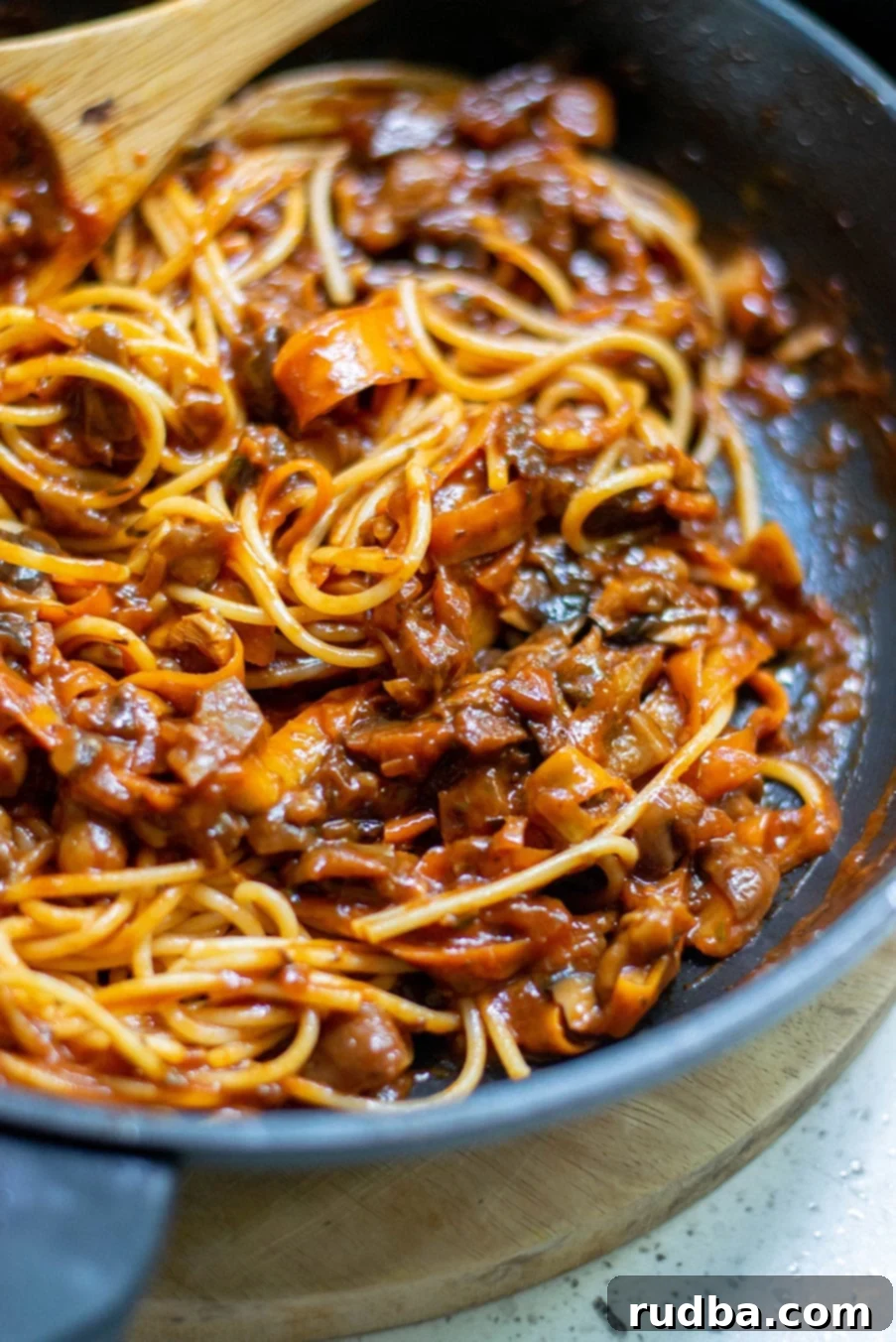 up close shot of spaghetti and mushroom bolognese sauce with a wooden spoon inside a black skillet. 
