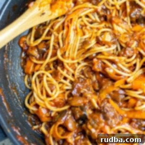 mushroom bolognese with pasta and a wooden spoon in a black skillet.