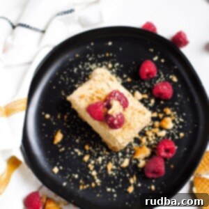 A perfectly squared slice of no-bake Dalgona cheesecake, ready to be served. It features a rich coffee-colored top layer and a creamy white base, hinting at its delightful texture.
