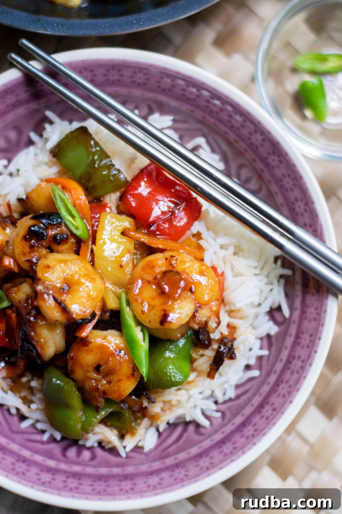 sweet and sour shrimp over white rice in a purple bowl with chop sticks on top.