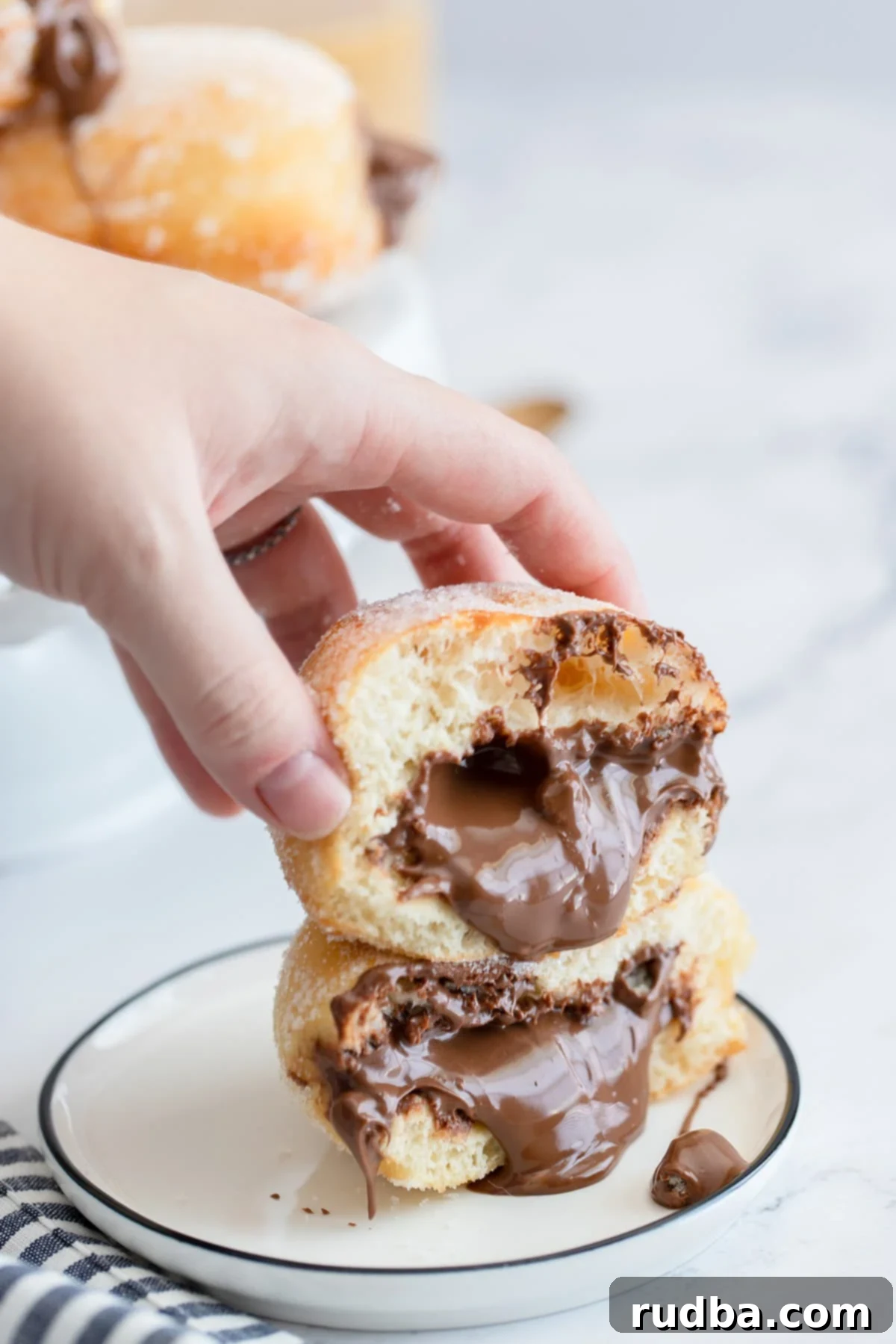 two nutella doughnuts on a small plate with nutella coming out of the donuts and a hand holding the donuts.