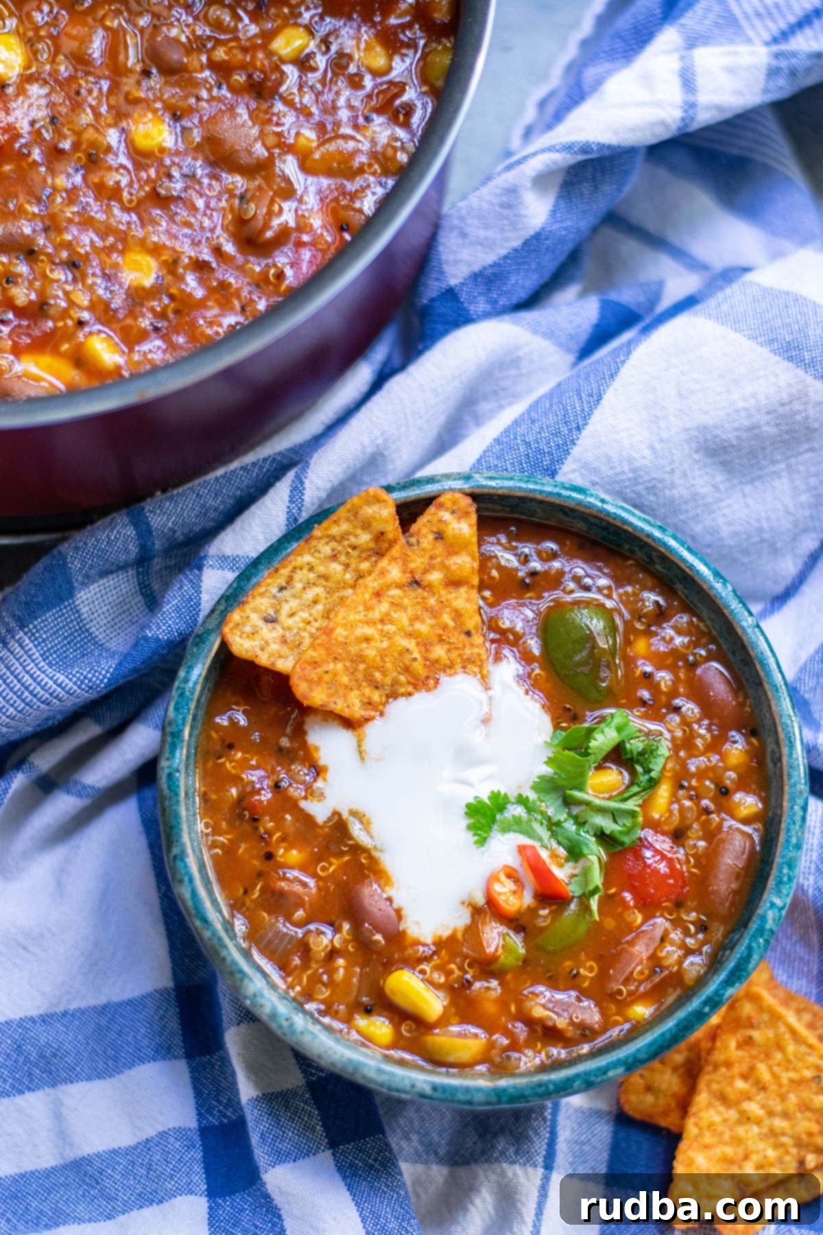 a small blue bowl filled with quinoa chili and dorito chips on the side and in the bowl. A pot with chili in the background and a blue towel underneath. 