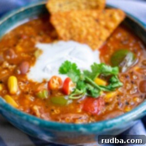 a bowl with quinoa chili, white cream on top, cilantro, and dorito chips on top of a blue towel.